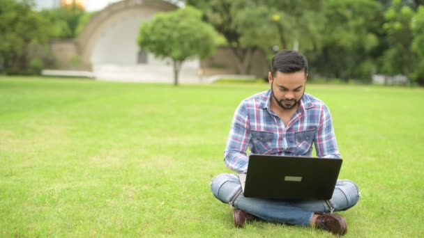 Joven guapo indio hombre en el parque usando ordenador portátil — Vídeos de Stock