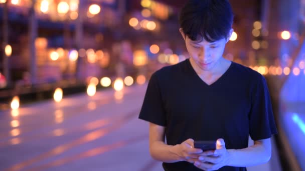 Retrato de hombre asiático al aire libre en la noche usando el teléfono móvil — Vídeos de Stock