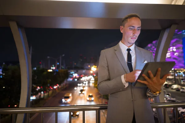 Молодой красивый бизнесмен на открытом воздухе ночью с помощью цифрового планшета — стоковое фото
