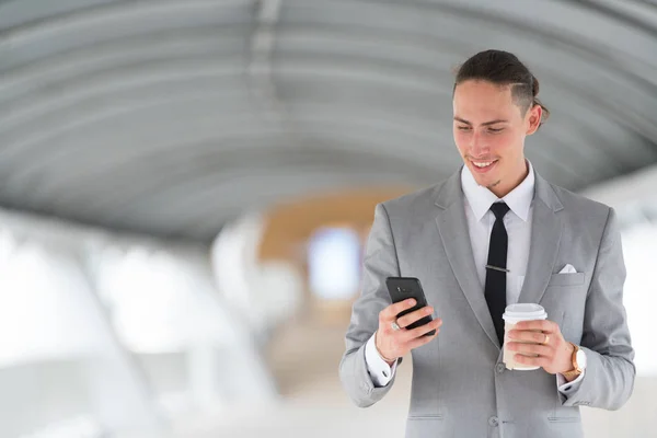 Бизнесмен с помощью телефона и проведение кофе Кубок на открытом воздухе — стоковое фото