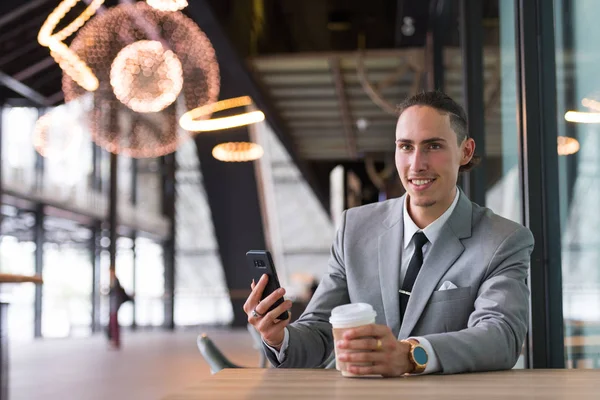 Бизнесмен сидит и использует мобильный телефон во время кофе — стоковое фото
