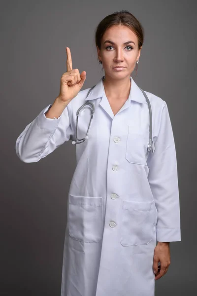 Joven hermosa mujer médico contra fondo gris — Foto de Stock