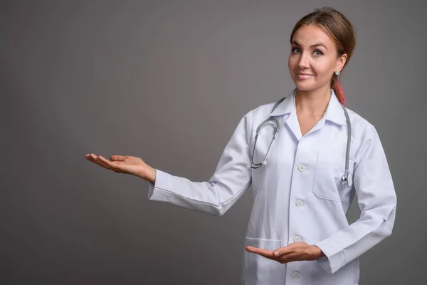 Joven hermosa mujer médico contra fondo gris — Foto de Stock