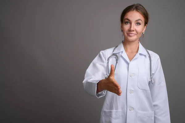 Joven hermosa mujer médico contra fondo gris — Foto de Stock