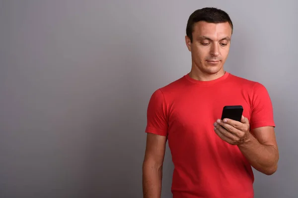 Uomo che indossa camicia rossa durante l'utilizzo del telefono cellulare contro la schiena grigia — Foto Stock
