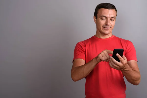 Человек в красной рубашке во время использования мобильного телефона против серой спине — стоковое фото