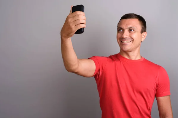 Muž na sobě červené tričko při používání mobilního telefonu proti šedé zpět — Stock fotografie