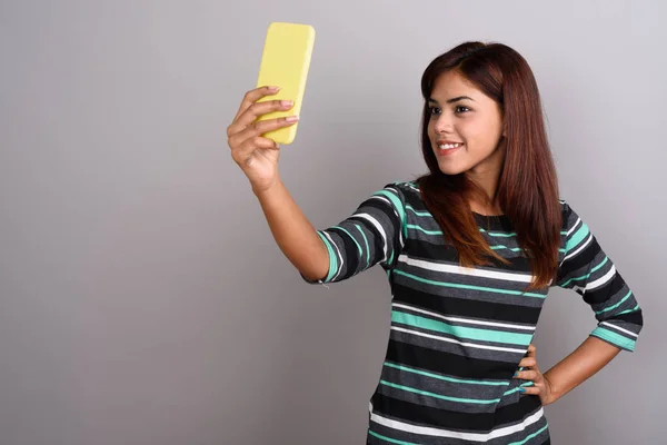 Молодая красивая индийская женщина использует мобильный телефон против серых баков — стоковое фото