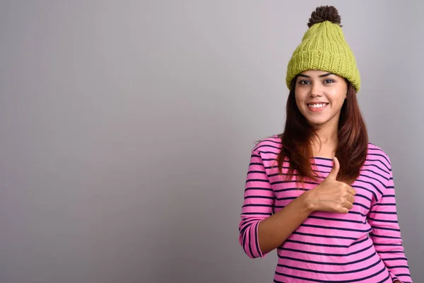 Junge schöne indische Frau mit Strickmütze gegen grauen Ba — Stockfoto