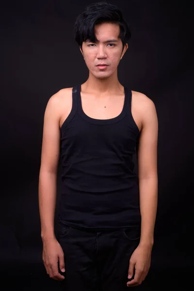 Young handsome Asian man against black background — Stock Photo, Image