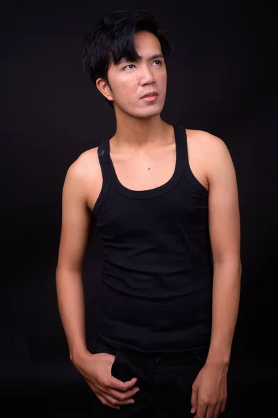 Young handsome Asian man against black background — Stock Photo, Image