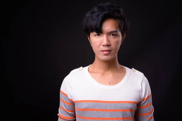 Young handsome Asian man against black background — Stock Photo, Image