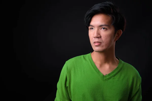 Young handsome Asian man against black background — Stock Photo, Image