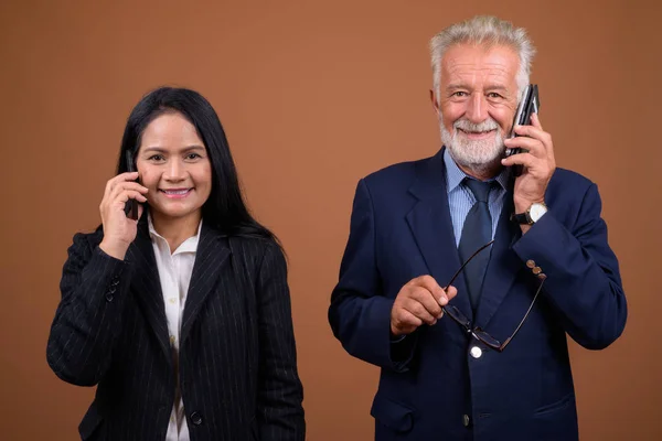 Mature multi-ethnic business couple against brown background — Stock Photo, Image