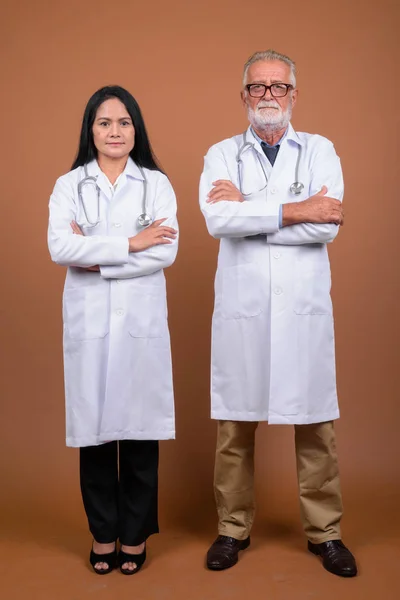Äldre multietniska par läkare mot brun bakgrund — Stockfoto