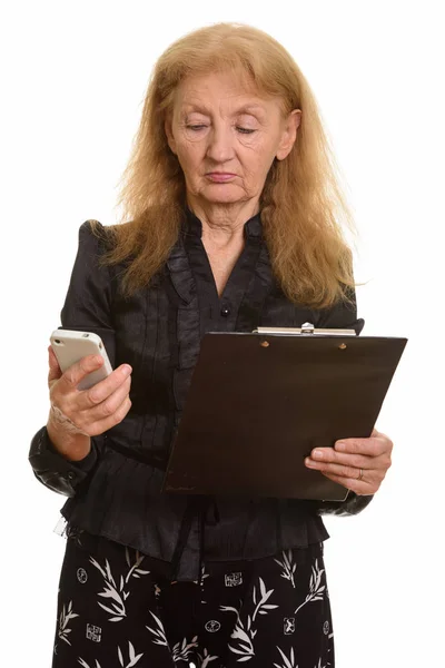 Studio shot of senior businesswoman holding clipboard while usin — Stock Photo, Image