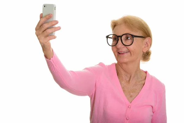 Счастливая пожилая женщина улыбается и делает селфи с помощью мобильного телефона — стоковое фото