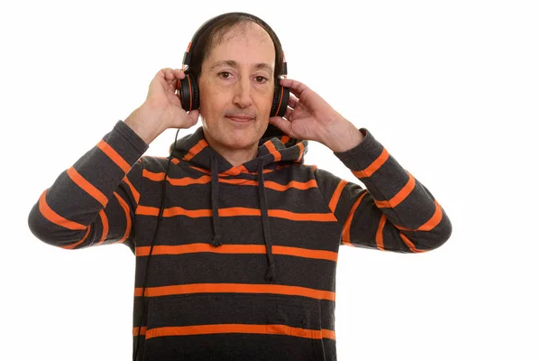 Studio shot of mature man holding headphones while listening to — Stock Photo, Image