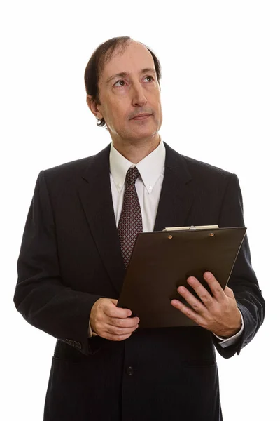 Studioaufnahme eines reifen Geschäftsmannes, der Klemmbrett hält, während er denkt — Stockfoto