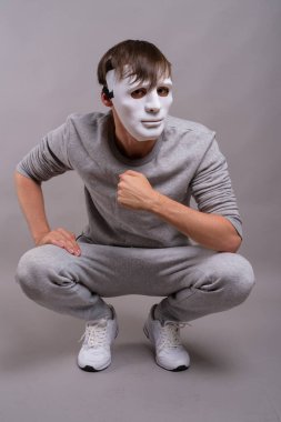 Gri arka planı çömelme sırasında beyaz Maske giyen genç adam stüdyo çekim