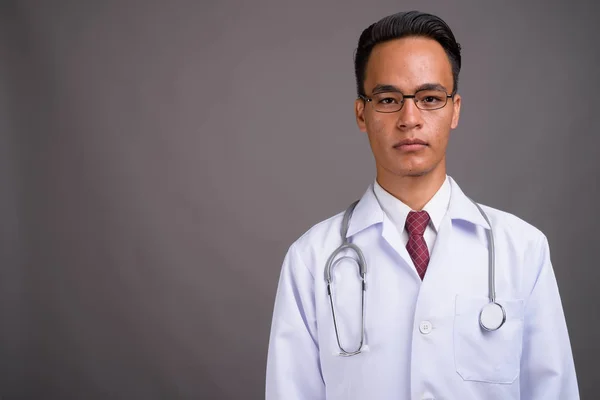 Молодой красивый индийский врач на сером фоне — стоковое фото