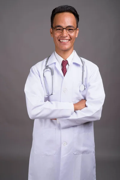 Junger hübscher indischer Arzt vor grauem Hintergrund — Stockfoto
