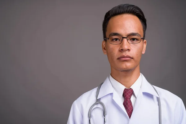 Молодой красивый индийский врач на сером фоне — стоковое фото