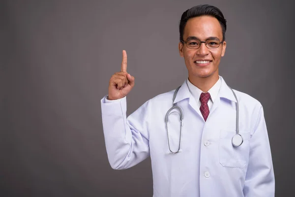 Young handsome Indian man doctor against gray background — Stock Photo, Image