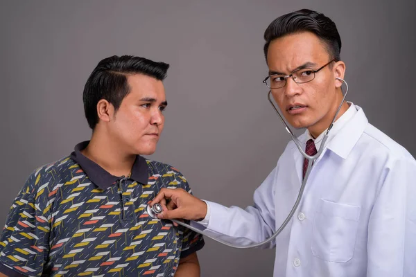 Joven hombre multiétnico y joven médico indio contra gris — Foto de Stock