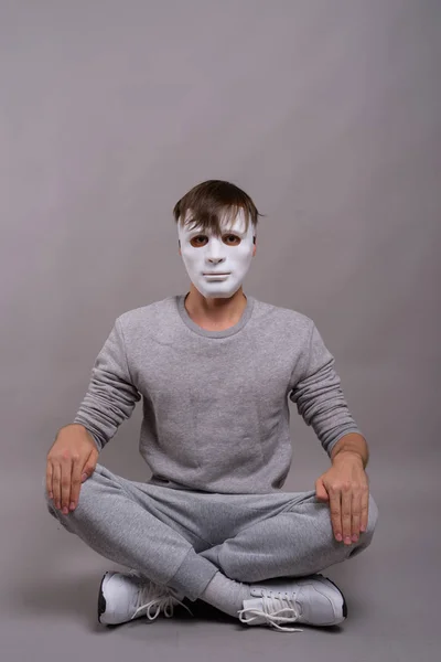 Jonge knappe man dragen witte masker tegen de grijze achtergrond — Stockfoto