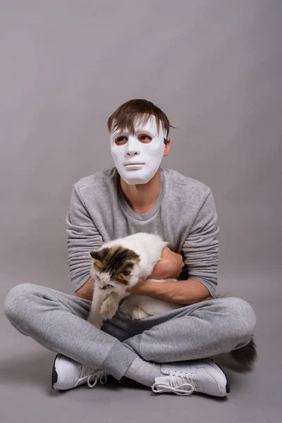 Jovem homem bonito vestindo máscara branca contra fundo cinza — Fotografia de Stock