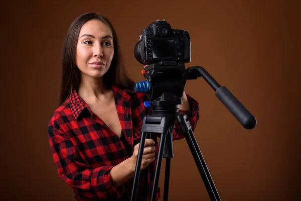 Studio shot of young beautiful woman vlogging against brown back — Stock Photo, Image