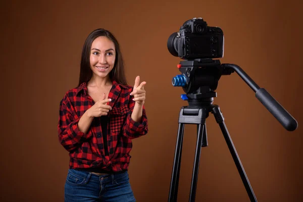 Studio shot van mooie jongedame vlogging tegen bruine rug — Stockfoto