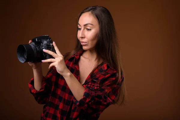 Studio shot van mooie jongedame met camera tegen bruin b — Stockfoto