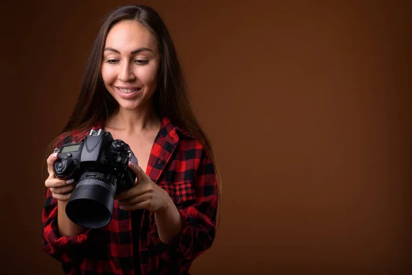 Studio shot van mooie jongedame met camera tegen bruin b — Stockfoto