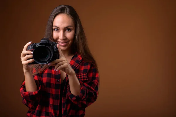 Studio shot van mooie jongedame met camera tegen bruin b — Stockfoto