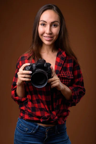 Estúdio tiro de mulher bonita jovem com câmera contra b marrom — Fotografia de Stock