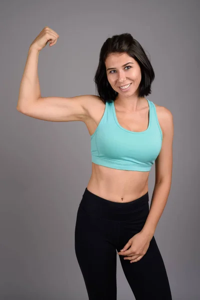 Young beautiful woman ready for gym against gray background — Stock Photo, Image
