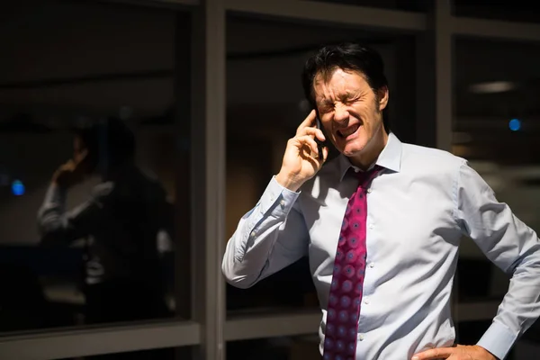 Estressado maduro empresário no escritório à noite falando no telefone móvel — Fotografia de Stock