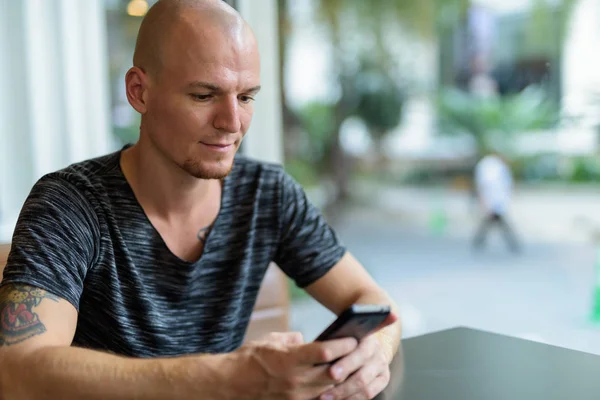 Young handsome bald man using mobile phone inside restaurant wit — Stock Photo, Image