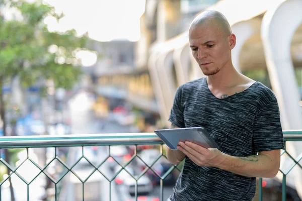 Young handsome bald man using digital tablet on the foot bridge — Stock Photo, Image