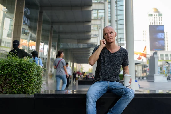 Young handsome bald man holding paper coffee cup while talking — Stock Photo, Image