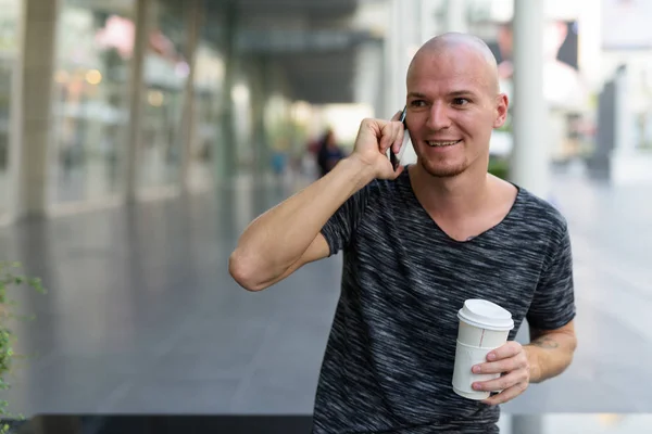 Thoughtful young happy bald man smiling and holding paper coffee — Stock Photo, Image