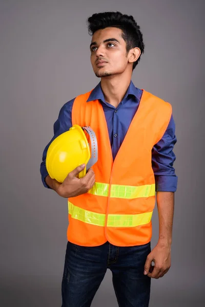 Joven trabajador de construcción indio contra fondo gris — Foto de Stock