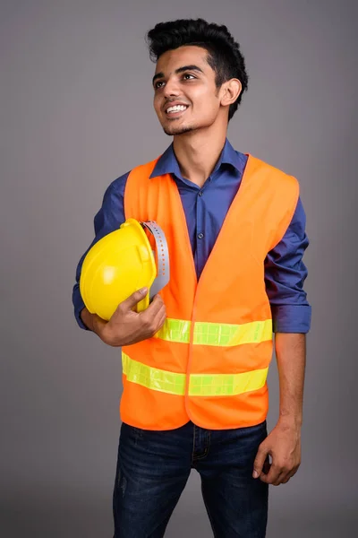 Joven trabajador de construcción indio contra fondo gris — Foto de Stock