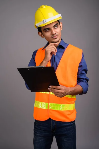 Joven trabajador de construcción indio contra fondo gris — Foto de Stock