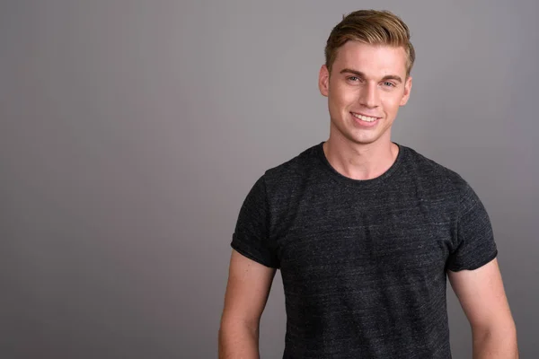 Joven hombre guapo con el pelo rubio usando camisa gris contra gr — Foto de Stock