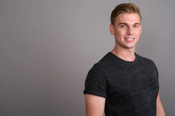 Joven hombre guapo con el pelo rubio usando camisa gris contra gr — Foto de Stock