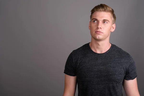 Young handsome man with blond hair wearing gray shirt against gr — Stock Photo, Image