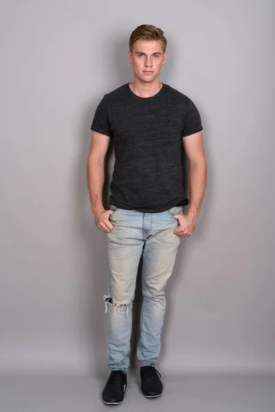Mladý pohledný muž s blond vlasy nosí šedé tričko proti gr — Stock fotografie